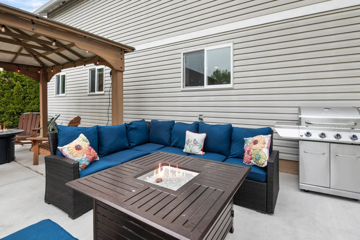 A spacious outdoor area with a sectional sofa, fire pit, grill, and a pergola, all arranged for groups to relax, socialize, and enjoy meals together. The scene conveys a fun, communal atmosphere ideal for celebrations and team-building activities.