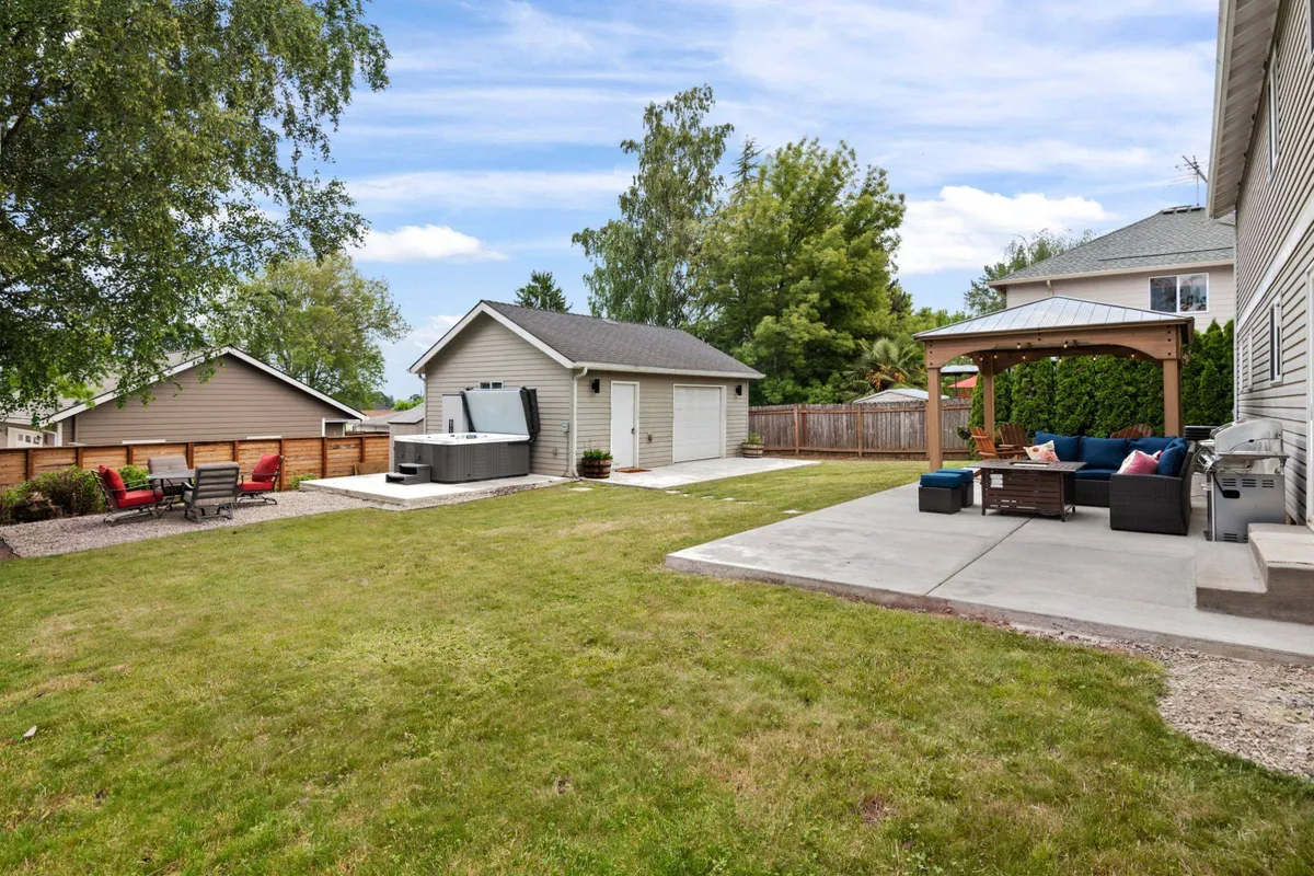 This image captures the spacious backyard featuring a lush green lawn, a hot tub, patio seating area, and a shed. The area is clearly designed for outdoor gatherings and relaxation, with ample space for pets and people alike.