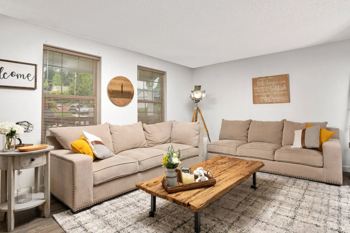 A cozy interior living room scene featuring a sofa, coffee table, wall art, and a welcome sign. The space feels warm and sociable, suggesting a comfortable environment for guests and their pets to gather, relax, or watch TV together.