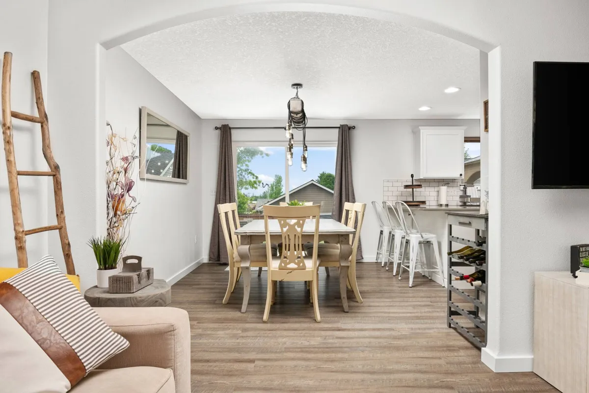 A cozy dining area with a welcoming table set beneath a stylish hanging light fixture. The layout includes a view into the living room, illustrating the open flow between social spaces. Large windows allow natural light to enhance the warm and inviting atmosphere.