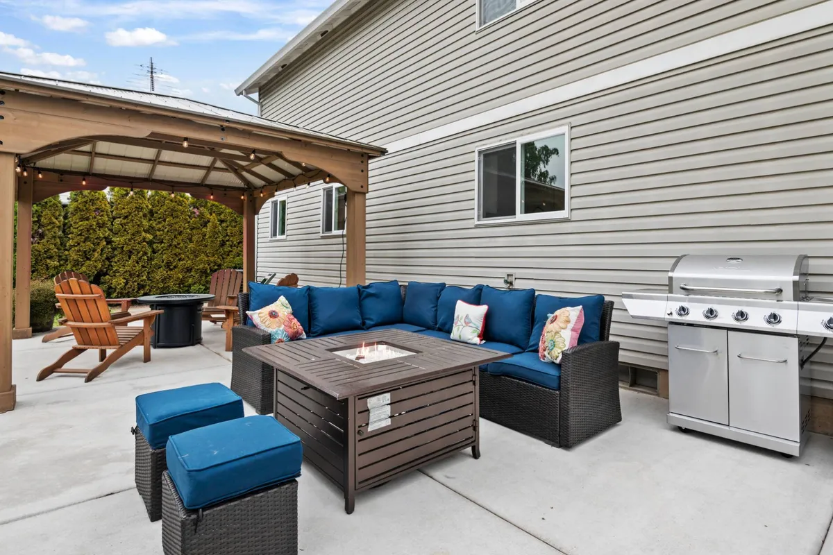 A welcoming outdoor seating area featuring a fire pit, grill, and pergola, set up for group gatherings. The scene suggests activities like barbecuing, relaxing, and socializing, with comfortable furniture arranged for conversation and connection.