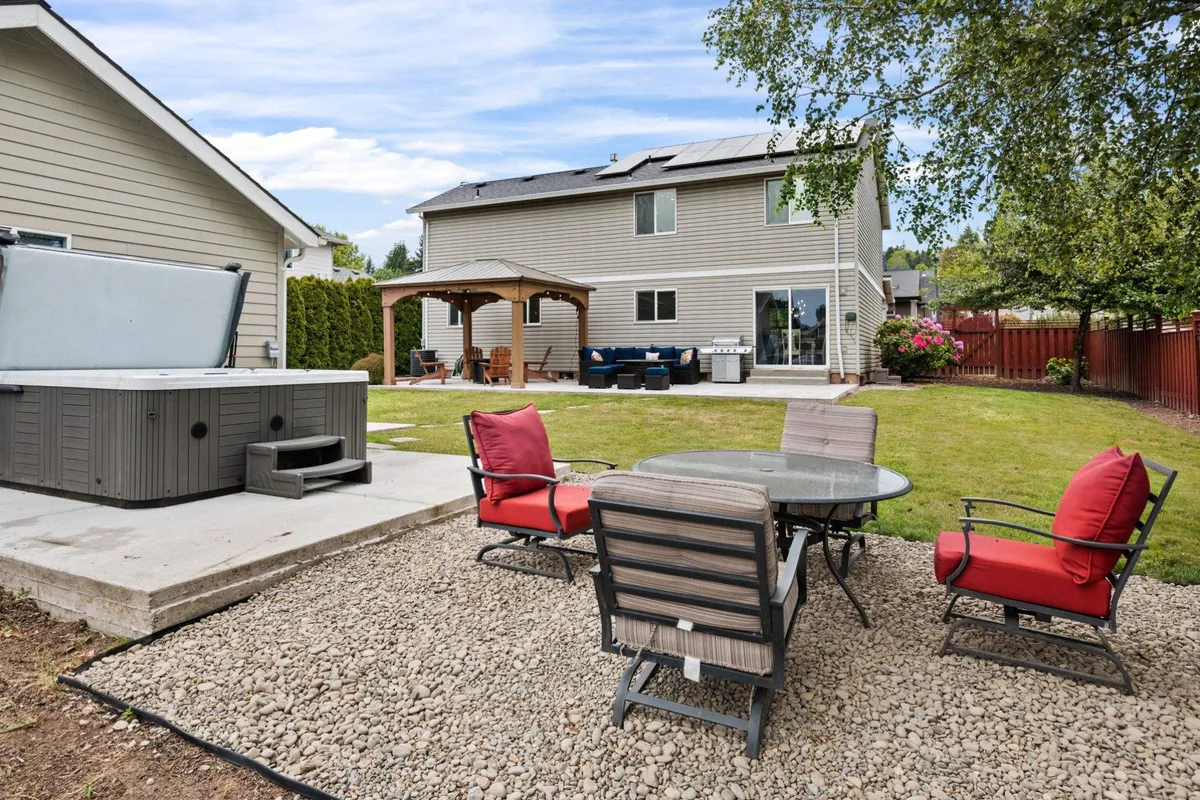 This image captures the inviting outdoor gathering space featuring a hot tub, a comfortable seating area, a charming gazebo, and a well-maintained lawn. The setup is perfect for group relaxation, informal meetings, and social hours, with sunset views and cozy ambiance.