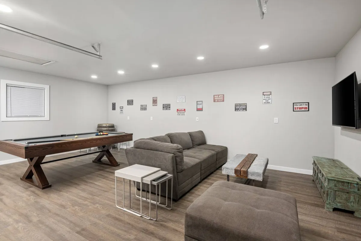 A bright, comfortable interior space showcasing a pool table, sofa, television, and playful wall signage. The room is perfect for group activities like game nights, movie marathons, or simply relaxing together.