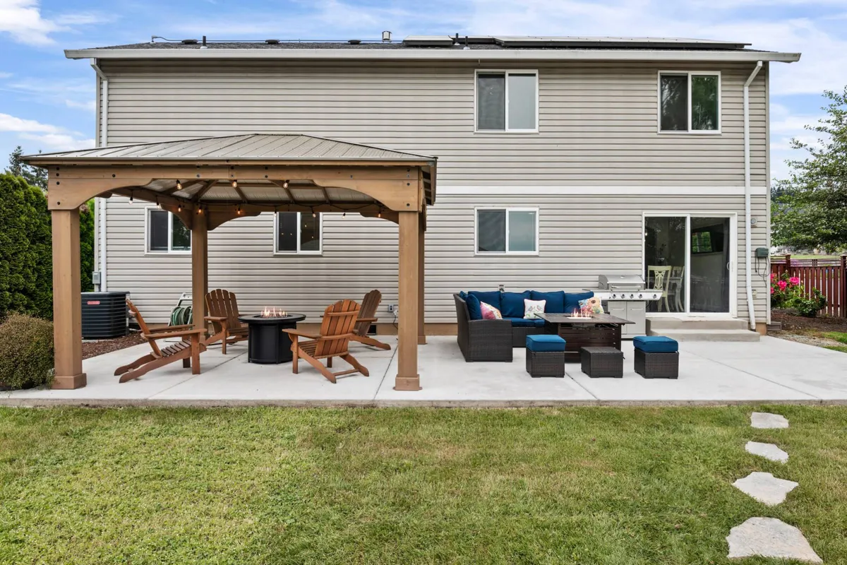 A comfortable outdoor seating area beneath a pergola, featuring a fire pit and a well-kept green lawn. The setting is designed for relaxed socializing and evening gatherings under the stars.